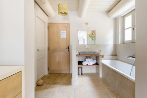 Ein Badezimmer mit Holztür, Spiegel, Waschbecken und Badewanne.