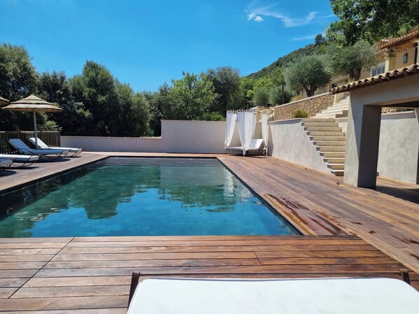 Ein Schwimmbecken mit Holzterrasse, Liegestühlen und einer Treppe zu einem überdachten Bereich.