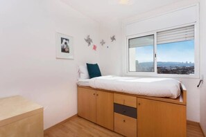 A bedroom with a bed, a window with a view, and a small cabinet. - Elegant Eixample Penthouse with Private Terrace & City Views (Barcelona)