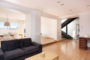 A modern living room with a sofa, a coffee table, and a staircase leading to another level. - Elegant Eixample Penthouse with Private Terrace & City Views (Barcelona)