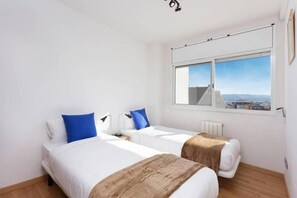 Ein Hotelzimmer mit zwei Betten, einem Fenster mit Blick auf die Stadt und einer Deckenleuchte.