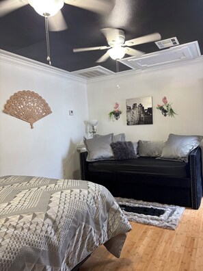 A bedroom with a bed, a black sofa, a decorative fan, and a cityscape painting. - Girls Night Out Downtown New Orleans (New Orleans)
