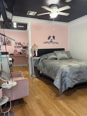 Un dormitorio con cama, tocador con espejo, una silla y ventilador de techo.