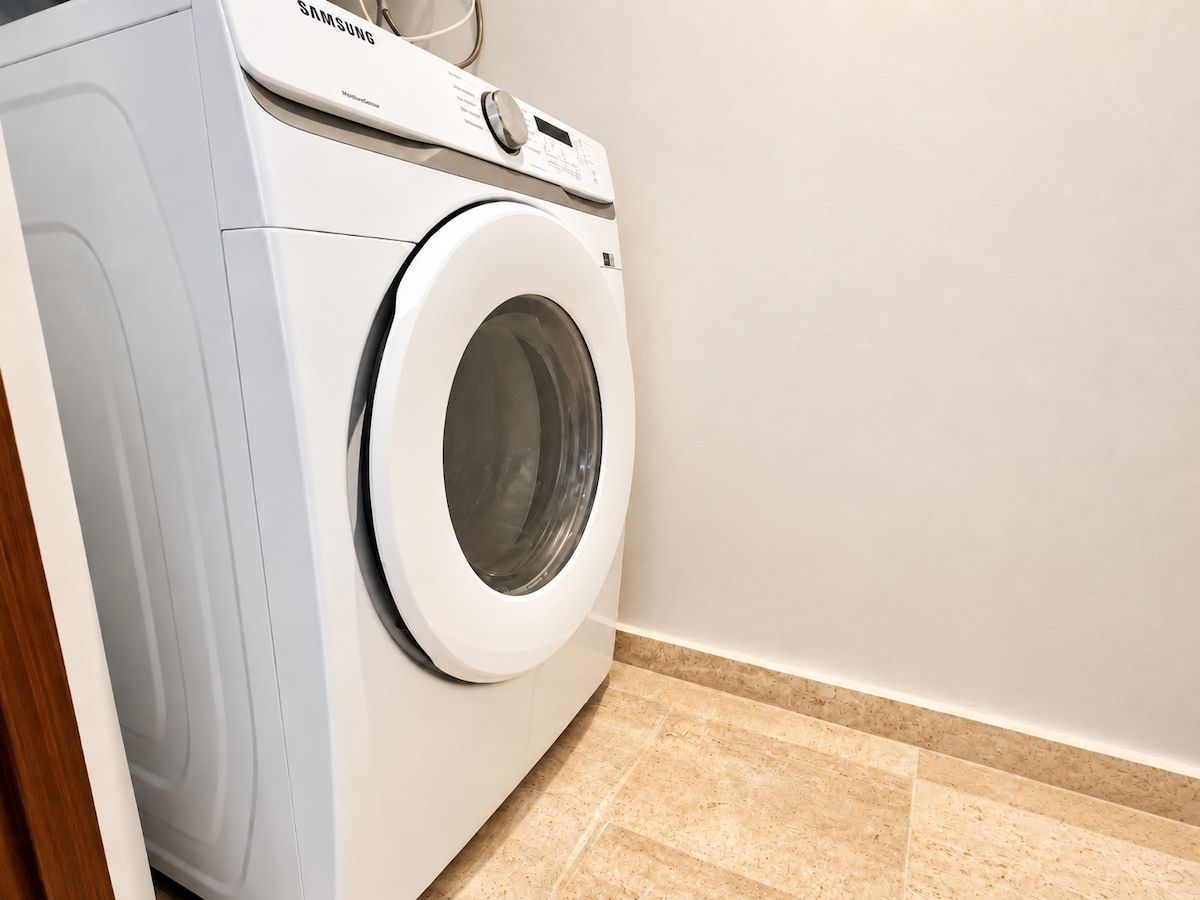 Eine Waschmaschine mit Frontlader steht in einer Ecke eines Raumes mit Fliesenboden.