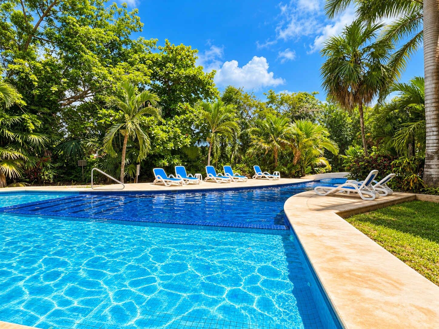 Ein Swimmingpool mit blauen Fliesen, umgeben von Palmen und Liegestühlen.