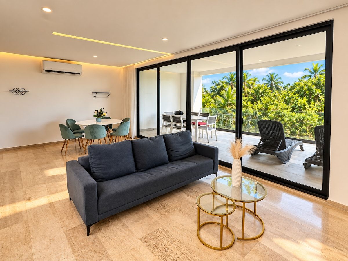 Una sala de estar moderna con un sofá, una mesa de centro de vidrio y vistas a un balcón con mobiliario exterior.