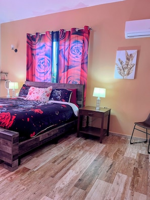 A bedroom with a wooden bed, two bedside tables with lamps, a large floral curtain, and an air conditioning unit on the wall. - Super Modern 3bd/3.5ba Spacious Villa Private pool, Grill Hispaniola Residencial (Cabarete)