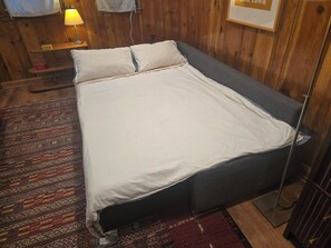Ein Einzelbett mit grauem Gestell und weißer Bettwäsche in einem Zimmer mit Holzwänden und einem gemusterten Teppich.