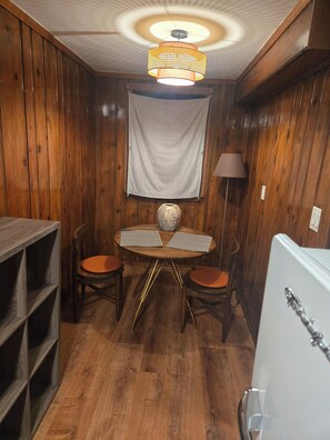 A room with wooden walls, a round table with chairs, a ceiling light fixture, and a white refrigerator. - Cozy Hyde Park Greystone Garden-Level Suite near Obama Presidential Center (Chicago)