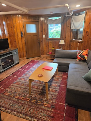 Um quarto aconchegante com sofá, mesinha, televisão e tapete estampado.