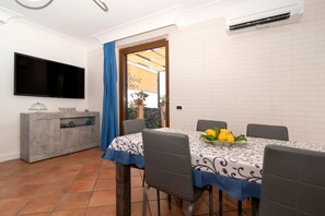A dining area with a table set for four, a flat-screen TV mounted on the wall, and a grey cabinet with a glass top. - Relais Cacace by Espresso Rentals (Massa Lubrense)