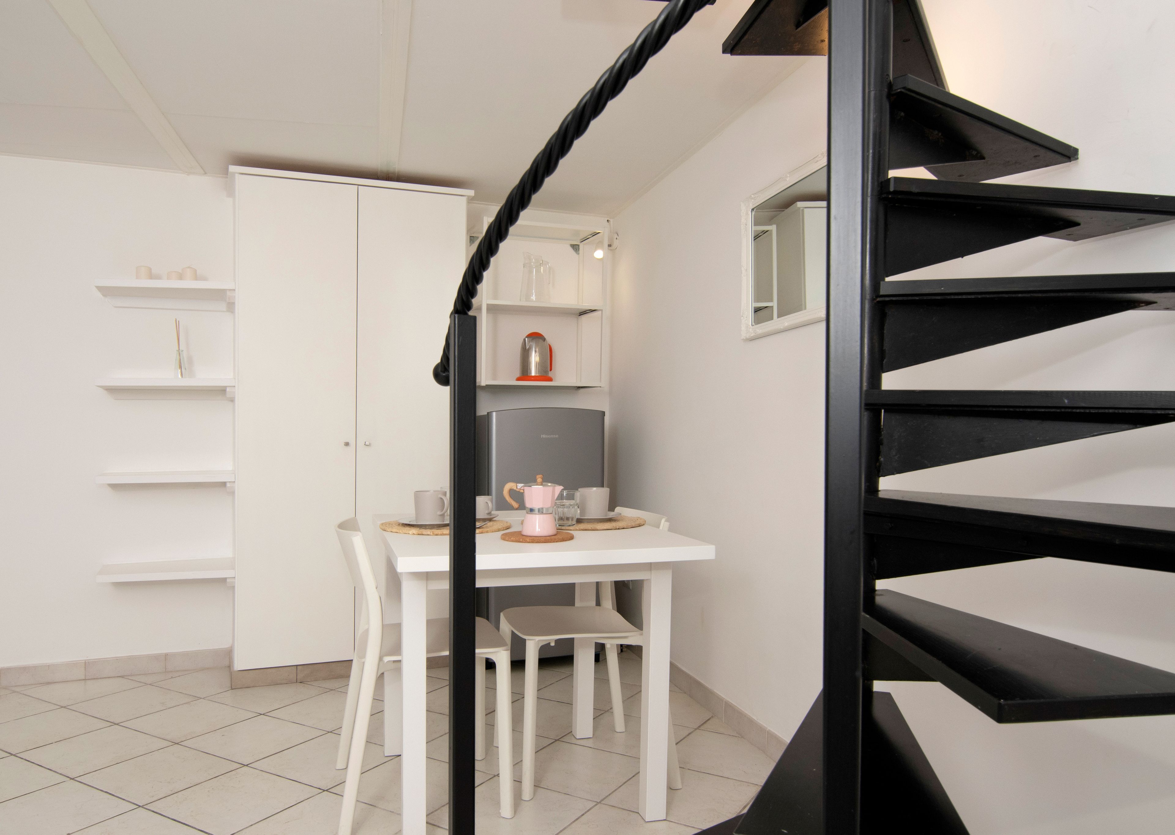 Eine Küche mit einem weißen Tisch, Stühlen, einer Kaffeemaschine und einem Kühlschrank.