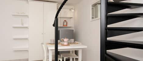 A kitchen with a white table, chairs, a coffee maker, and a refrigerator.
