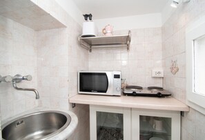 A compact kitchen with a microwave, a small stove, a sink, and a shelf with a kettle. - Casa Melina by Espresso Rentals (Sant'Agata Sui Due Golfi)