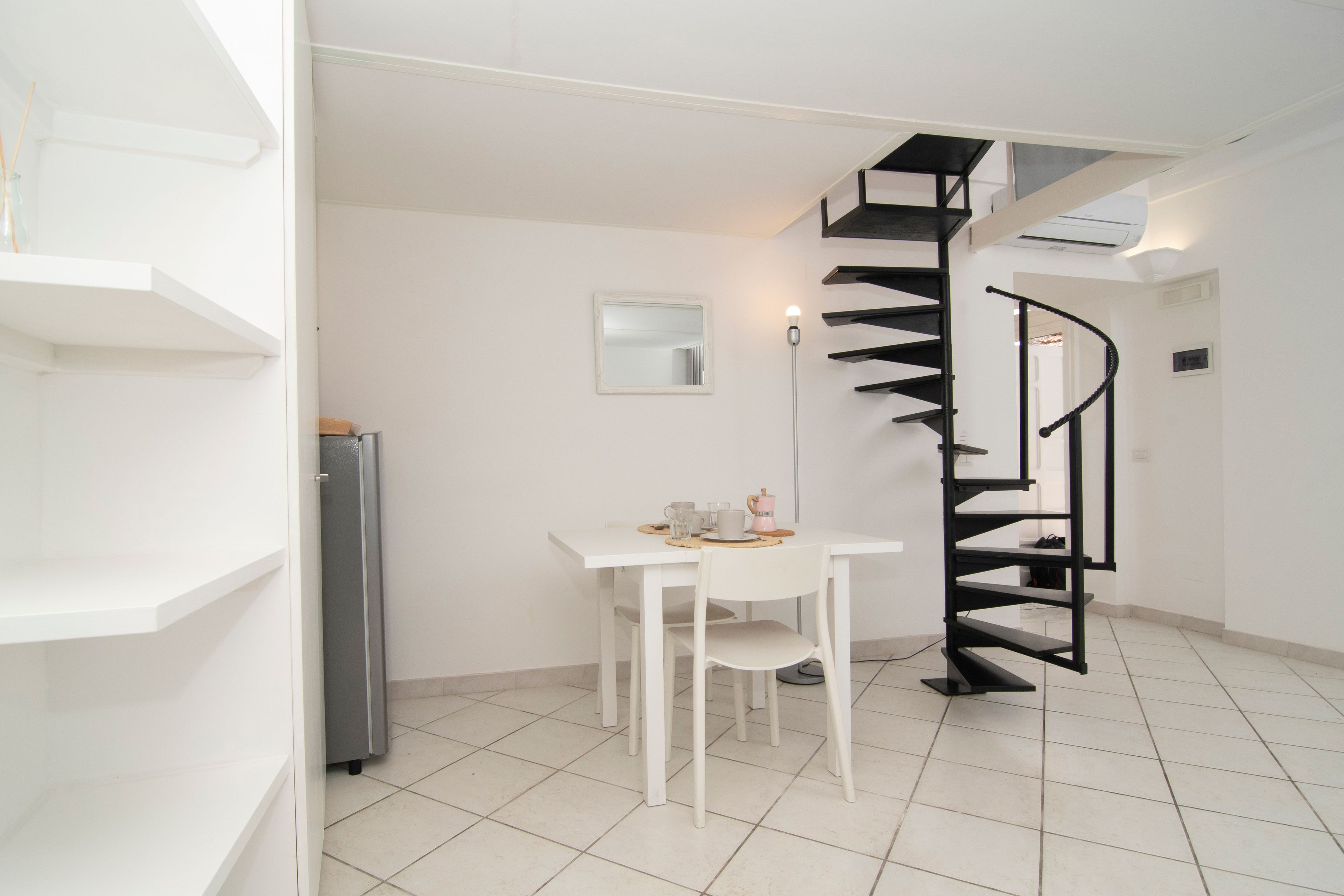 Une cuisine moderne avec des meubles blancs, un four encastré et un escalier en colimaçon noir.