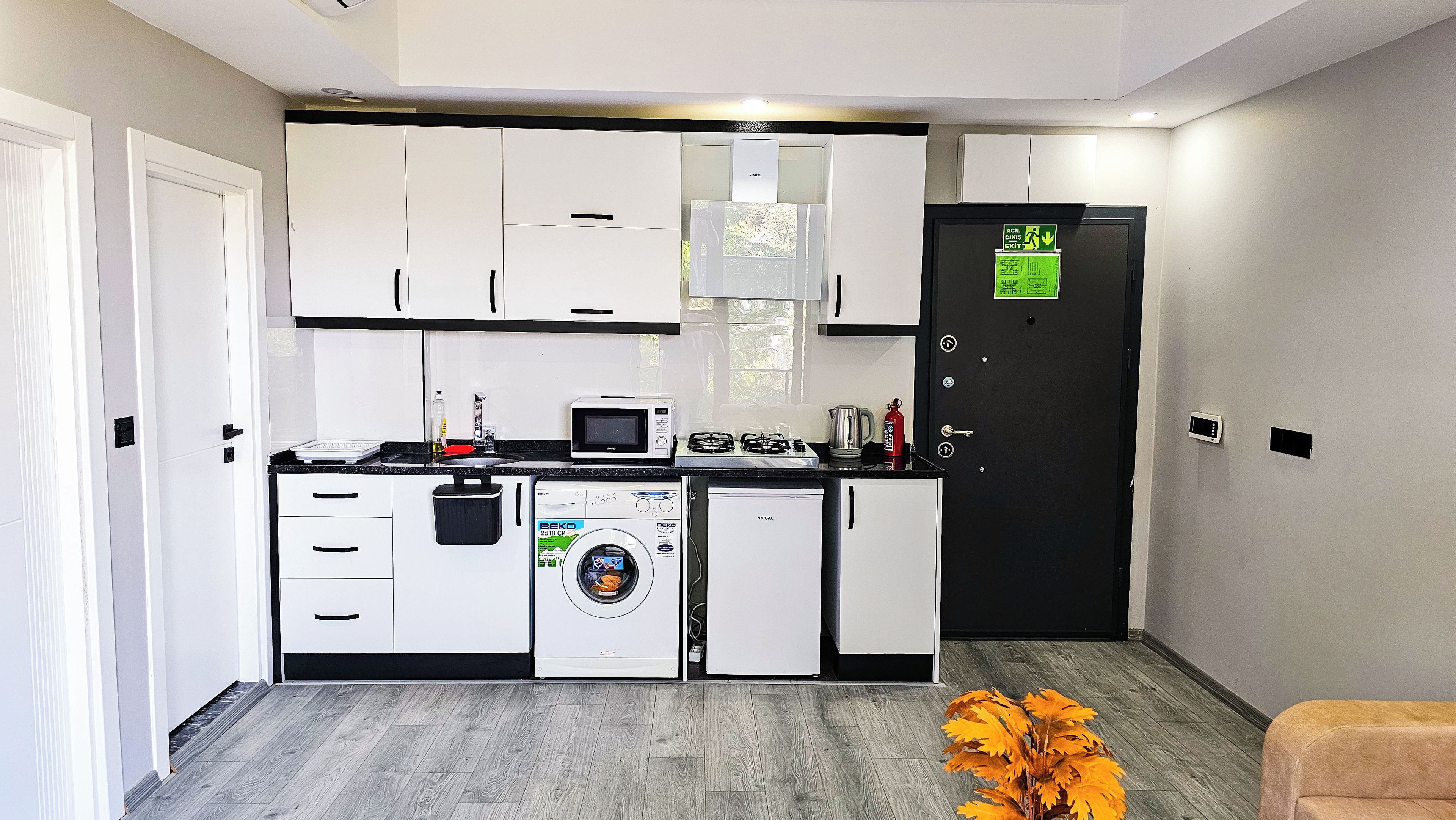 Una cocina compacta con armarios blancos, microondas, cafetera y lavadora.