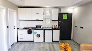 Een compacte keuken met witte kastjes, een magnetron, een koffiezetapparaat en een wasmachine.