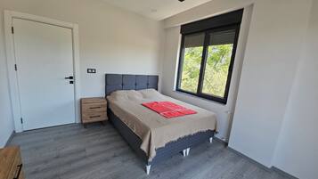 Un dormitorio con cama, mesita de noche, ventana y puerta.