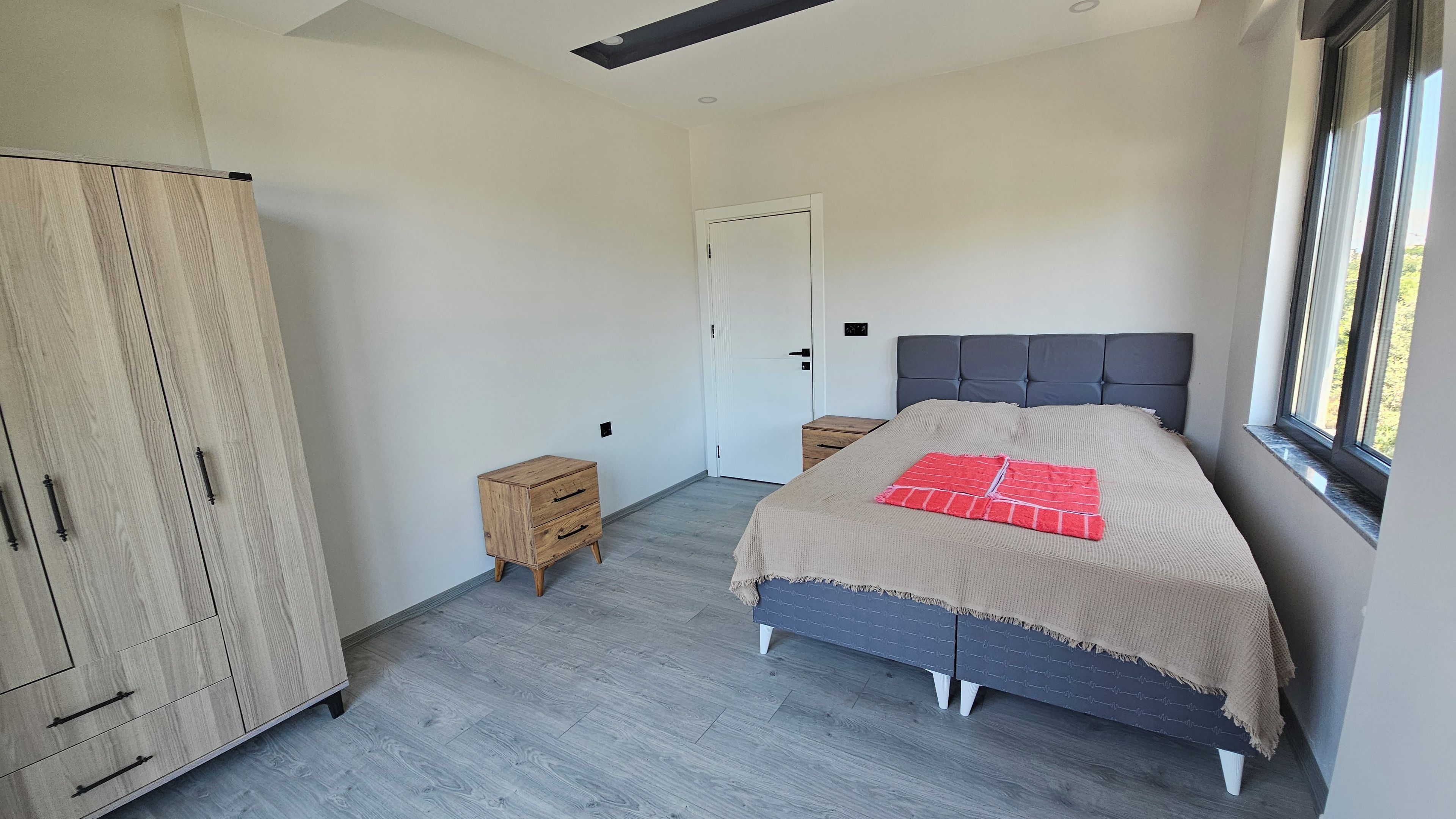 Een slaapkamer met een bed, een kledingkast, nachtkastjes en een raam.