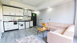 A modern kitchen with built-in appliances, a sofa, and a small table with a plant. - The Mini Antalya Holiday Flat (Muratpaşa)