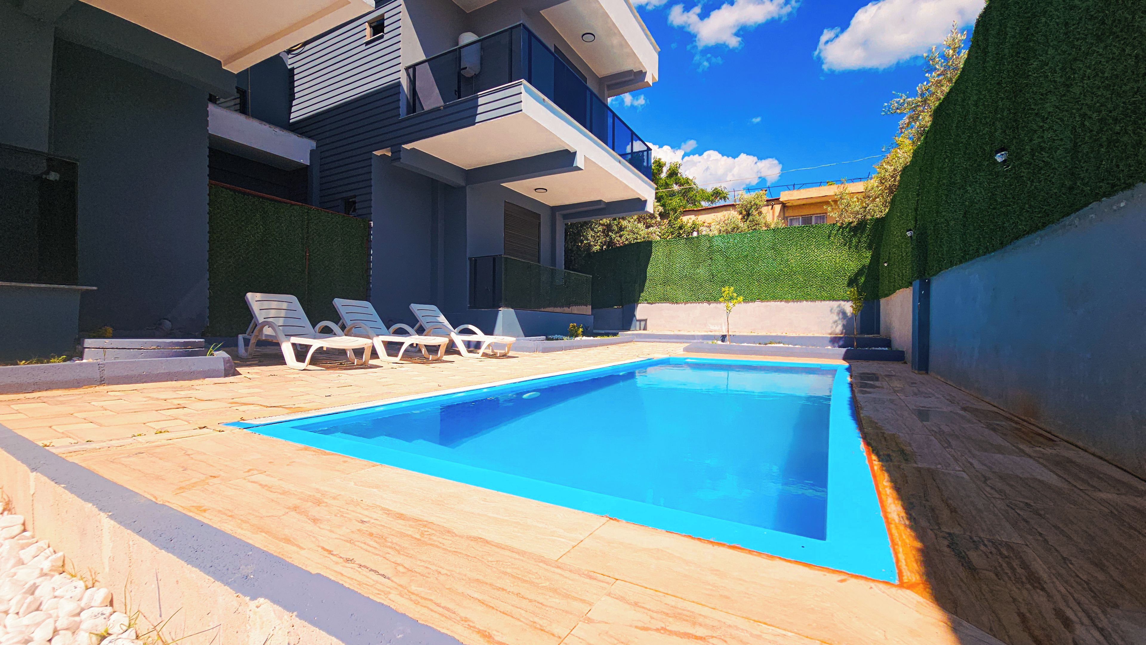 A modern swimming pool with lounge chairs, surrounded by a paved deck and a hedge.