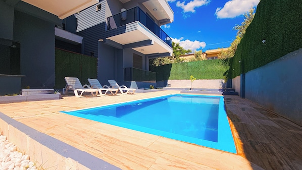 A modern swimming pool with lounge chairs, surrounded by a paved deck and a hedge.