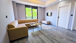 Een moderne woonkamer met een beige modulaire bank, een salontafel met decoratieve objecten, een aan de muur bevestigde televisie en een deur.