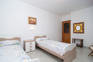 A bedroom with two single beds, a bedside table with drawers, a nightstand with a lamp, a wooden door, and a wall-mounted mirror. - Villa Antolusa by Espresso Rentals (Priora)
