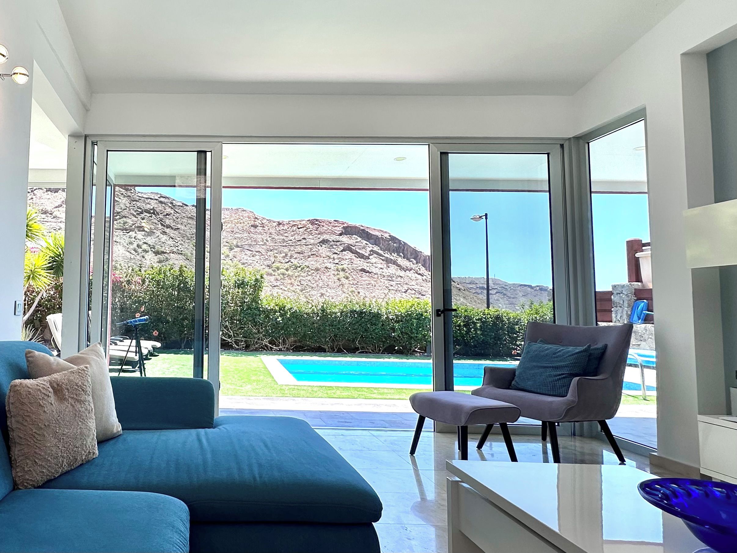 A modern living room with a sofa, a chair, and a view of a pool and mountains.