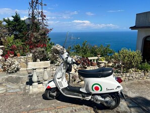 A white Vespa scooter parked on a stone-paved area with a view of the sea and a clear sky. - Villa Fontanarosa by Espresso Rentals (Massa Lubrense)