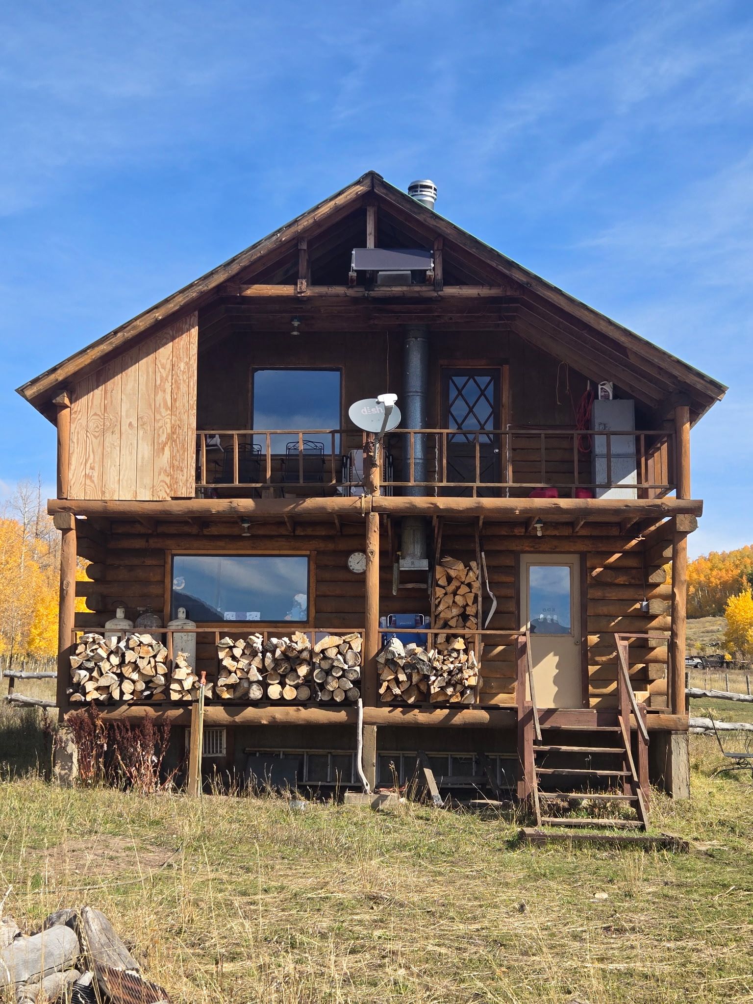 A two-story log cabin with a balcony, large windows, and a chimney.