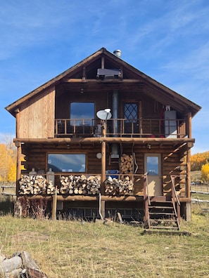 A two-story log cabin with a balcony, large windows, and a chimney. - Rustic 3-Bedroom Off-Grid Cabin at the Base of Electric Mountain (Paonia)