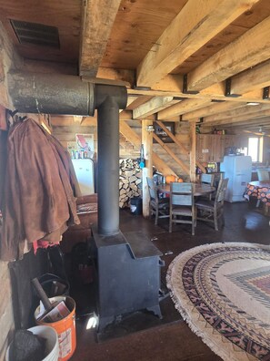 A rustic interior with a wood-burning stove, a dining table with chairs, and a patterned rug. - Rustic 3-Bedroom Off-Grid Cabin at the Base of Electric Mountain (Paonia)