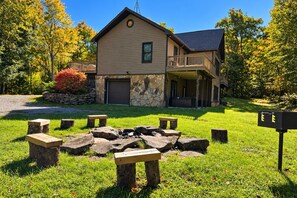 A two-story house with a stone facade, a balcony, and a stone fire pit with benches. - Private 4 Acres, Hot Tub, Fire Pit, 2 Mi to Snowshoe Entry (Cass)