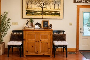 A wooden cabinet with two chairs, a framed painting, a calendar, and a door with a sign. - Private 4 Acres, Hot Tub, Fire Pit, 2 Mi to Snowshoe Entry (Cass)