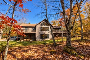 A two-story house with a balcony, surrounded by trees with autumn leaves. - Private 4 Acres, Hot Tub, Fire Pit, 2 Mi to Snowshoe Entry (Cass)