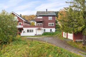A two-story house with a white garage door, a red exterior, and a gravel driveway. - Tromsø 80 m² Apartment with balcony sea view (Tromsø)