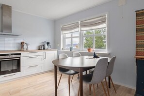 Une cuisine moderne avec un coin repas, des meubles blancs, un four encastré et une grande fenêtre offrant une belle vue.