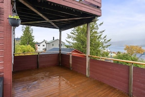 Une terrasse en bois dotée d’un espace abrité, offrant une vue sur un quartier résidentiel et un plan d’eau.