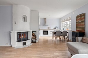 A modern living room with a fireplace, a dining area with chairs, and a kitchen in the background. - Tromsø 80 m² Apartment with balcony sea view (Tromsø)