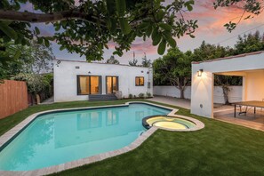 Ein Garten mit Swimmingpool, Terrassenbereich und einem Haus mit weißer Fassade.