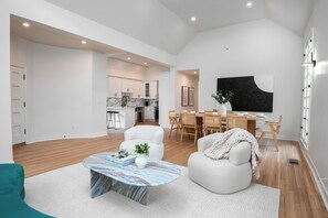 Ein modernes Wohnzimmer mit einem Marmortisch, einem weißen Sessel und einem Essbereich mit Holzkohle und einem schwarz-weißen abstrakten Gemälde.
