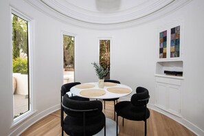 A room with a round table, black chairs, a vase with plants, and a white cabinet with a stained glass window. - Alta Vista Terrace By Alora Reserve (Los Angeles)