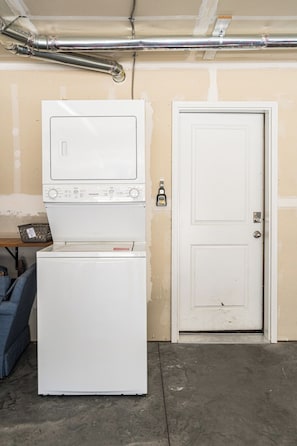 Une buanderie équipée d’un lave-linge et d’un sèche-linge, avec une porte et des conduits apparents.
