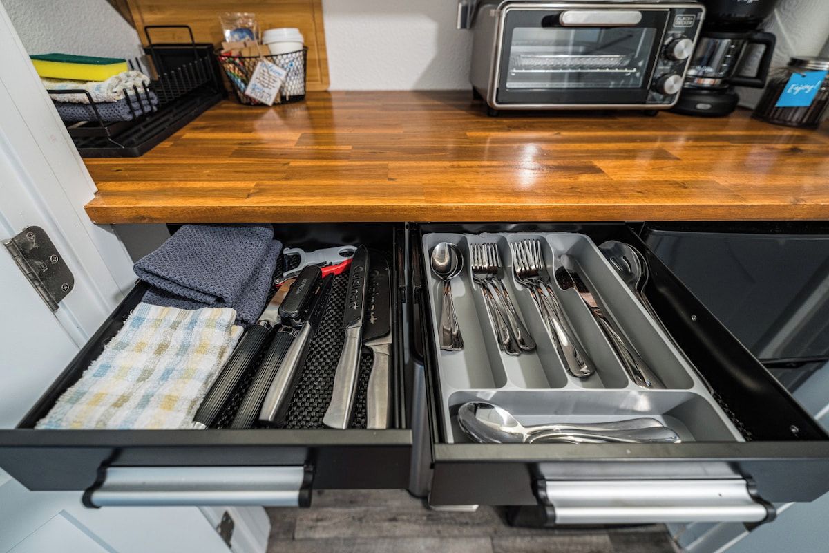 A kitchen drawer with utensils and a toaster oven on a wooden countertop.