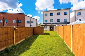 A residential area with a grassy yard, wooden fences, and modern buildings in the background. - Gemstone Diamond - Coop LIVE - Etihad - Free Parking - Pool table (Greater Manchester)