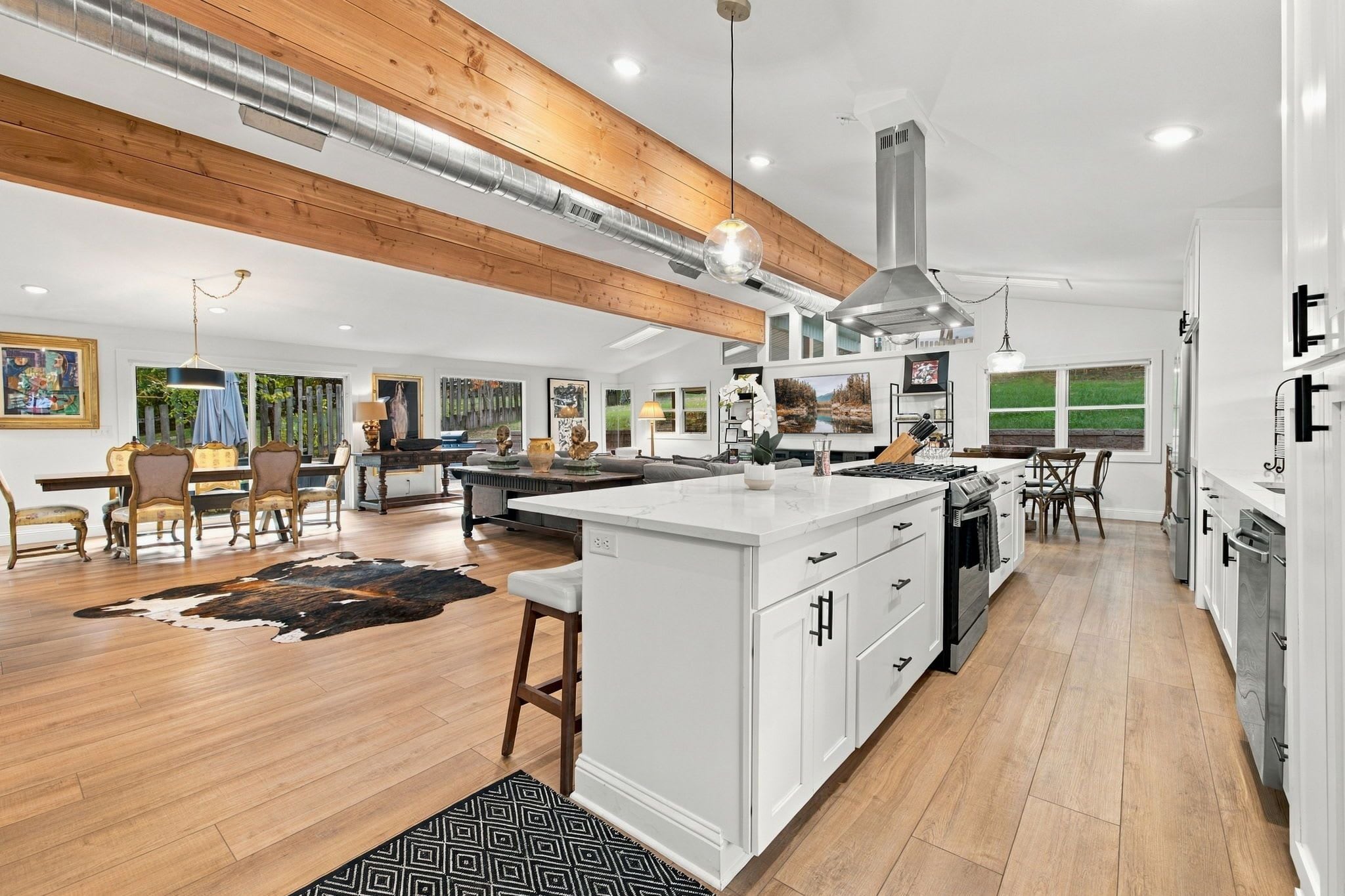 A spacious kitchen with a central island, wooden beams, and a large window.
