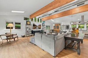 A spacious living area with a large grey sofa, wooden flooring, and a high ceiling with exposed beams. - Sunset - 0.8 miles to Razorback Stadium (Fayetteville)