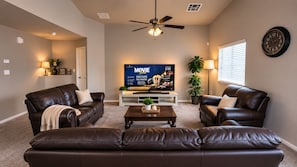A living room with a flat-screen TV, leather sofas, a coffee table, and a ceiling fan.