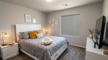 Un dormitorio con cama, mesitas de noche, televisor y ventana con persianas.